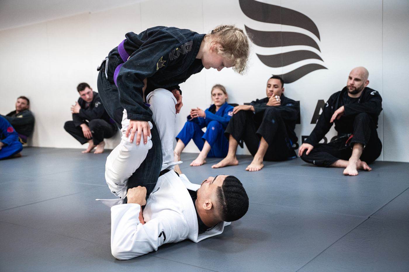 Eine Frau mit lila Gürtel passiert die Guard ihres Partners, die Gruppe sitzt vor dem Dream-Art-Logo und schaut zu