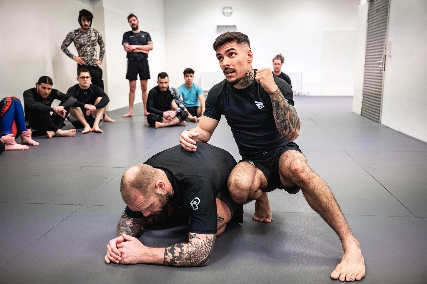 Trainer zeigt im NoGi-Training eine Kontrolle, die Gruppe schaut zu